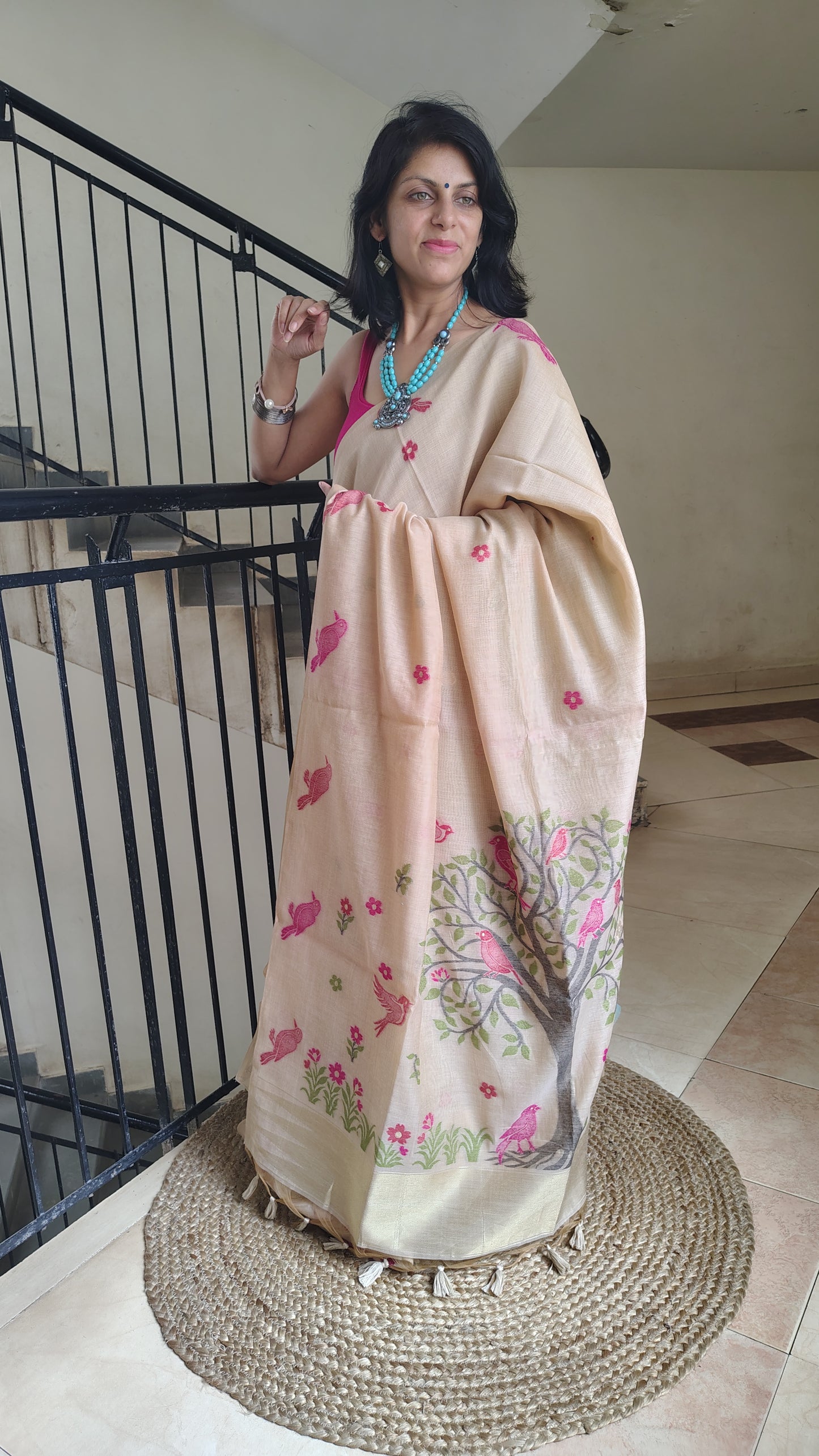 Woman wearing a beige saree with floral patterns in an indoor setting.